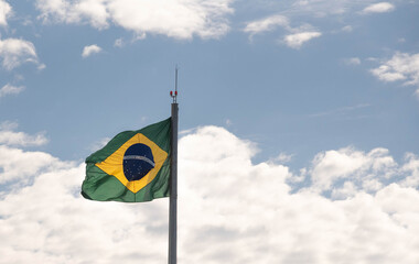 Brazilian flag flying and in the background the blue sky with white clouds
