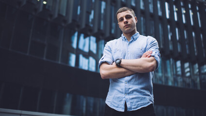 Calm young male manager standing on street with folded arms