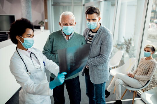 Senior man and his adult son examining X-ray with black female doctor at the clinic.