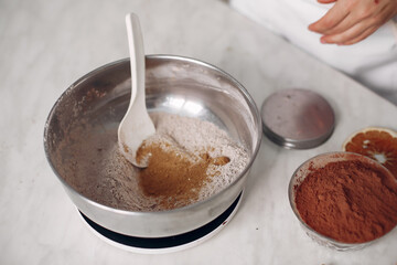 Woman poured cocoa into a bowl. Confectioner mixes the ingredients. Lady is preparing dessert.