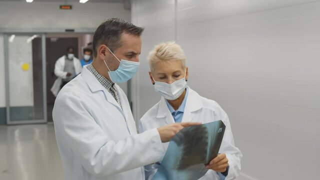 Doctors in protective mask discussing an x-ray of lungs in hospital corridor