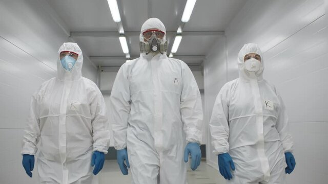 Team of virologists in hazmat suits walking in corridor to do disinfection