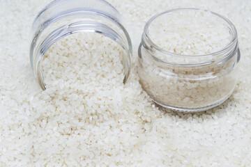 White round rice in two glass jars. Scattered rice as food background.