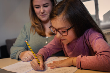 Mother helps her daughter with homework sitting at the living room table at home.