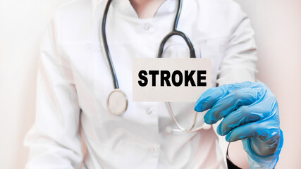 The doctor's blue - gloved hands show the word STROKE - . a gloved hand on a white background. Medical concept. the medicine