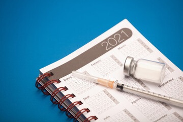 syringe and vaccine canister, with calendar 2021, blue background