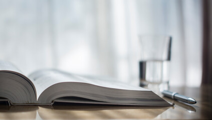 A large open book on the table. A pen on the desk.