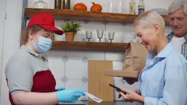 Courier in safety mask and gloves delivering food to senior couple