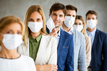 Business man taking off hisprotective facial mask and looking at the camera with histeam members standing in the line