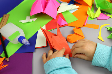 Child makes origami crafts from colored paper, hands close-up