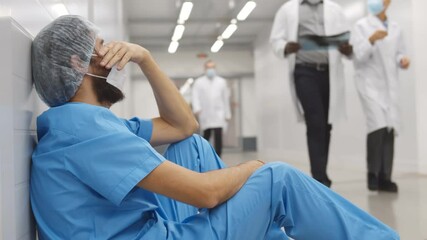 Colleagues supporting and cheering surgeon sitting on floor in hospital corridor