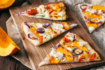 Pieces of tarte flambee with pumpkin, red onions and cheese on a wooden board