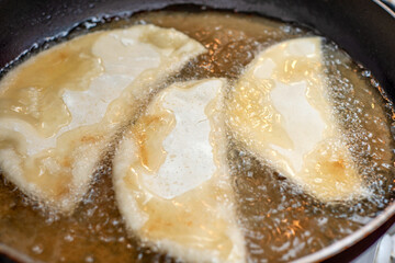 Almost ready pasties are fried in hot oil in a pan.