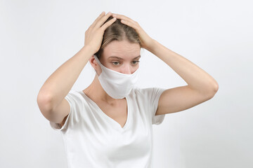 Young blond woman in virus disposable face mask  keeping raised hand on her head expressing feelings, sadness, worried. Protection for covid-19