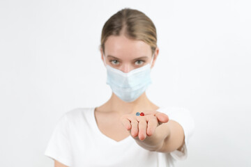 An young white woman in virus disposable face mask holding pills in front of her. White background...