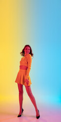 Beautiful seductive girl in fashionable, romantic yellow outfit on gradient yellow-blue background in neon light. Full-length portrait. Copyspace for ad. Summer, fashion, beauty, emotions concept.