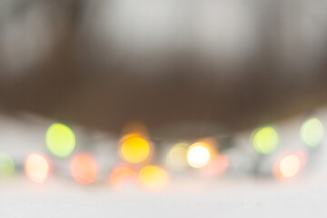 Christmas background with bokeh from a colored garland on the snow in the forest. New Year decor on a frosty day