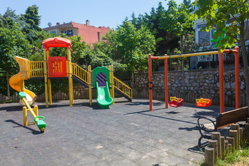 Colorful and empty playground in the park among the houses. Children run, slide, swing,seesaw on modern playground. Urban neighborhood childhood concept.