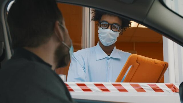 Man in car wearing safety mask making order in drive thru window