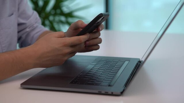 Business person typing on his laptop and picking up the smartphone in an office. Businessman writing a message on computer and mobile phone.