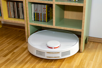Weißer Staubsaugerroboter / Saugroboter reinigt im Wohnzimmer den Parkettboden / Laminat  - kommt...