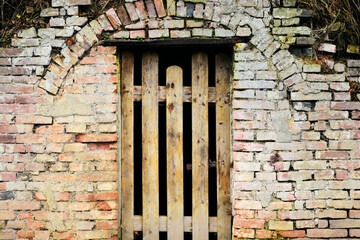 An old wooden gate in a rustic brick wall that is half derelict with a round arch