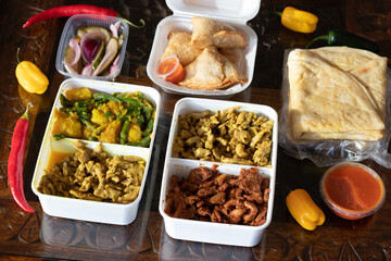 Curry, roti, potatoes, Indian and surinam food inside a take away plastic over a rustic table
