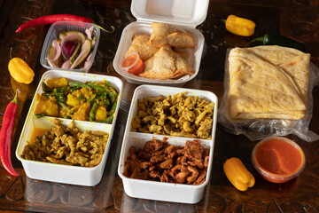  Indian and surinam food inside a take away plastic over a rustic table
