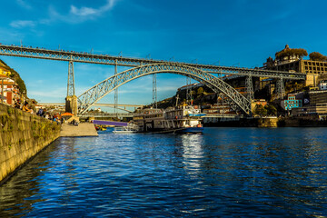 Fototapeta na wymiar Tourist cruiser sets sail beneath the Dom Luiz bridge in Porto, Portugal on a late sunny afternoon