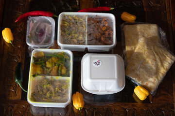 Curry, roti, potatoes, Indian and surinam food inside a take away plastic over a rustic table
