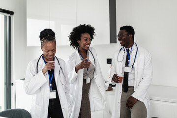 Fototapeta premium Group of three African American doctors relaxing and smiling in hospital rest room. They are talking and drinking coffee.