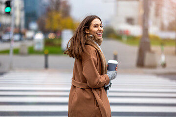 Young woman walking on the city street holding cup of coffee

