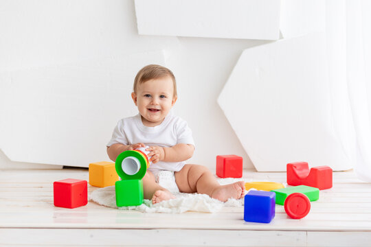 happy little baby six months old in a white t shirt and diapers playing at home on a Mat in a bright room with bright colored cubes