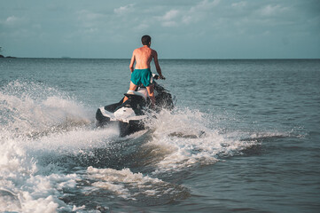 man on his back on the jet ski passing over a wave into the sea, at sunset