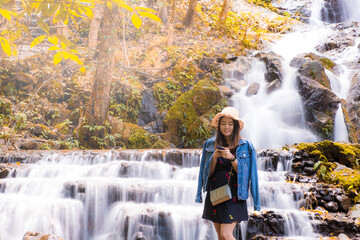 Asian woman alone smiling and waering hat in Autumn waterfalls beautiful scenery in Chiang Mai , Thailand