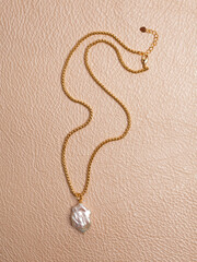 Luxury elegant baroque pearl pendant with golden chain on beige leather background