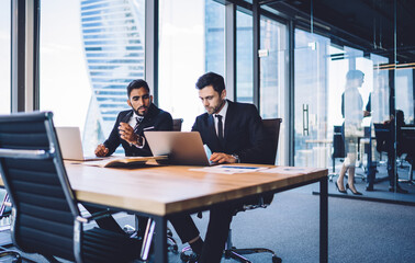 Multiracial business colleagues discussing tutorial video watching on modern laptop technology, successful male partners in formal clothes browsing banking application connecting to office internet