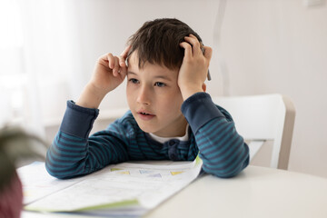 Portrait of young boy struggling with his homework at home. Children home education concept. Distance learning