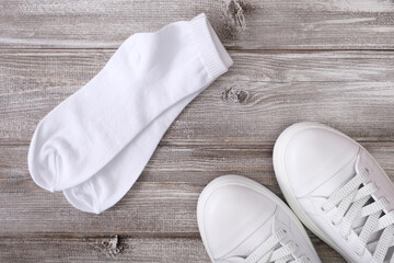 White leather sneakers and white cotton socks on wooden background, a set for walking and workout