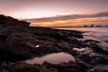 Obraz premium Stunning sunset from a rocky beach in Cabo de Palos with La Manga del Mar Menor skyline in the background, Murcia, Spain