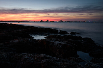 Obraz premium Stunning sunset from a rocky beach in Cabo de Palos with La Manga del Mar Menor skyline in the background, Murcia, Spain
