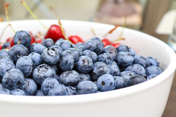 Raw juicy berries of sweet cherry and blueberry in a white ceramic dish, close up