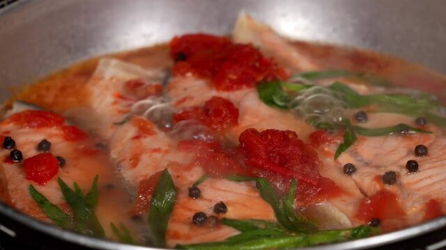 Salmon fish boiling in water with tarragon herbs, tomatoes and black pepper in a saucepan.