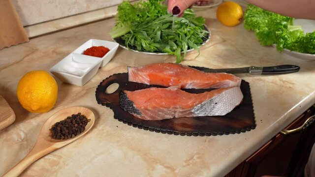 Woman's hand pours salt on two pieces salmon fish.