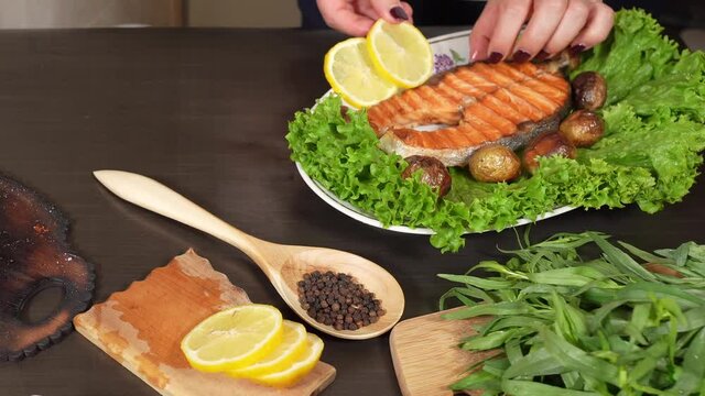 Woman's hand adds slised lemons on the fried salmon on the plate with lettuce