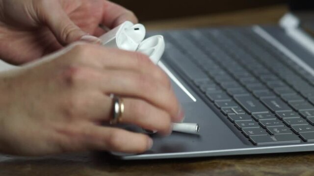 Womans hands on the bureau taking out the wireless earpods from case to the laptop. Computer, headphones ready to start home office work.