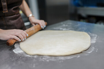 Close up of woman's hands rolling dough in bakery with rolling pin