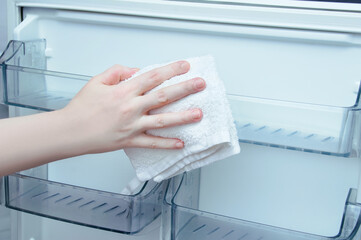 Caucasian woman hand with a cotton rag washes the refrigerator door.