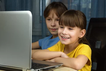 Poster Twee gelukkige meisjes kijken naar de laptop en glimlachen. Concept van thuisonderwijs op afstand. © Albert Ziganshin