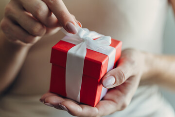 Close-up of female hands holding a small gift wrapped with a satin ribbon